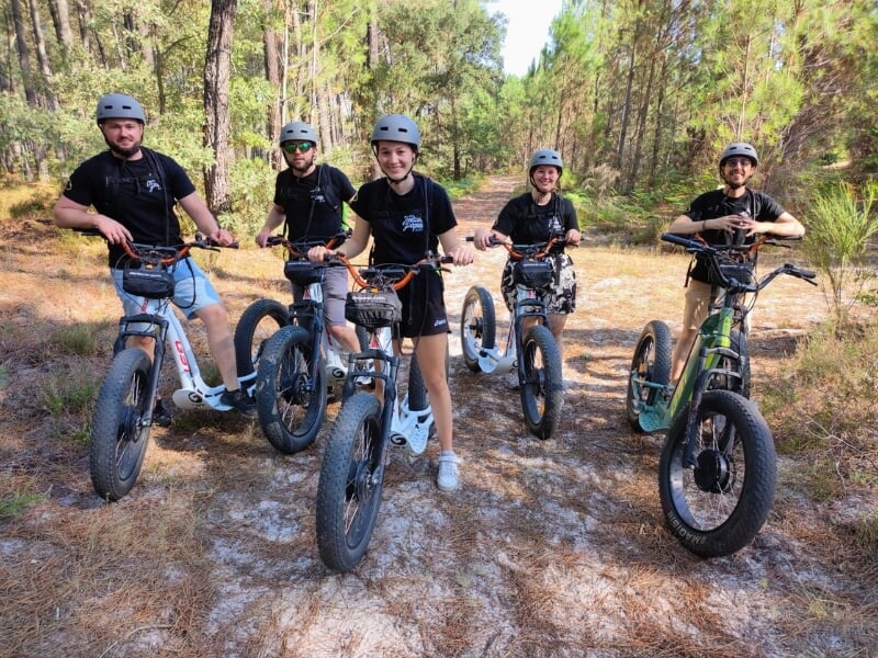 Un groupe pilotant des trottinettes électriques tout-terrain pose sur un chemin forestier.