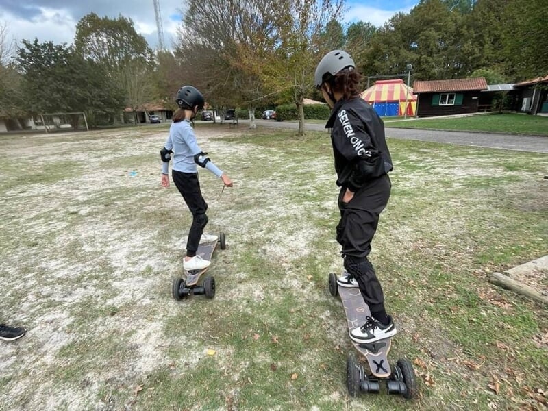 Deux personnes glissent sur des skates électriques sur un sol herbeux.
