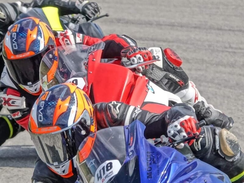 Des motocyclistes en course rapprochée sur une piste, concentrés dans un virage, avec un gros plan sur un motocycliste en combinaison rouge et blanche et un autre en bleu.