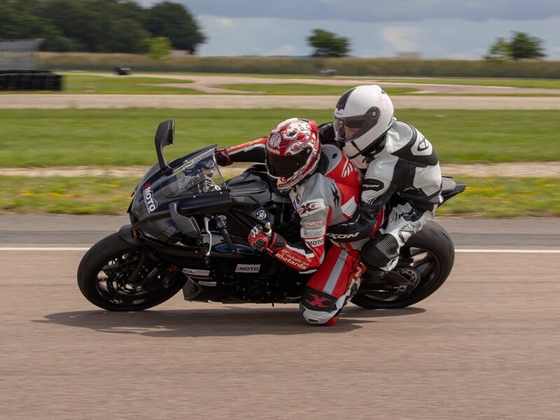 Moto noire en action sur la piste, deux pilotes inclinés dans un virage serré.