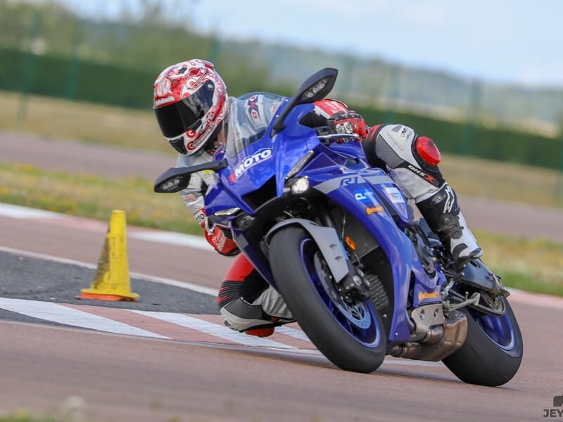 un pilote avec un casque rouge se couche dans un virage de circuit sur une moto bleue