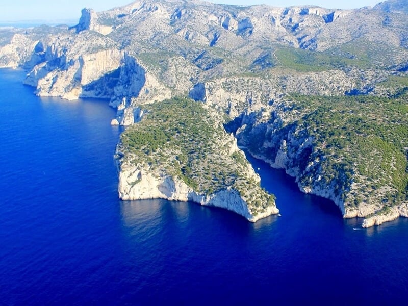 Vue aérienne des falaises et des criques de la Calanque de Sugiton près de Marseille, avec la mer Méditerranée d'un bleu profond en contraste avec la végétation verte et les formations rocheuses