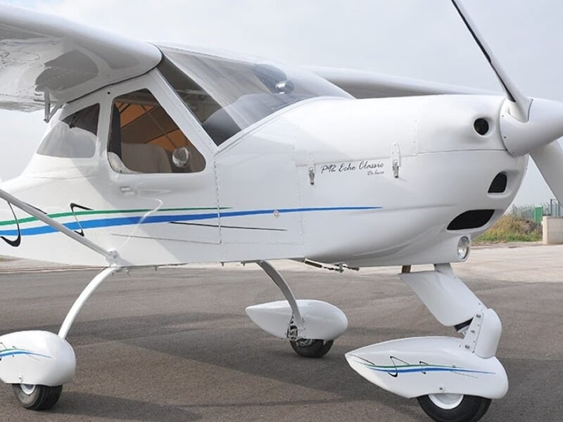 Avion léger blanc stationné sur une piste d'aviation, mettant en évidence les détails et la structure de l'appareil