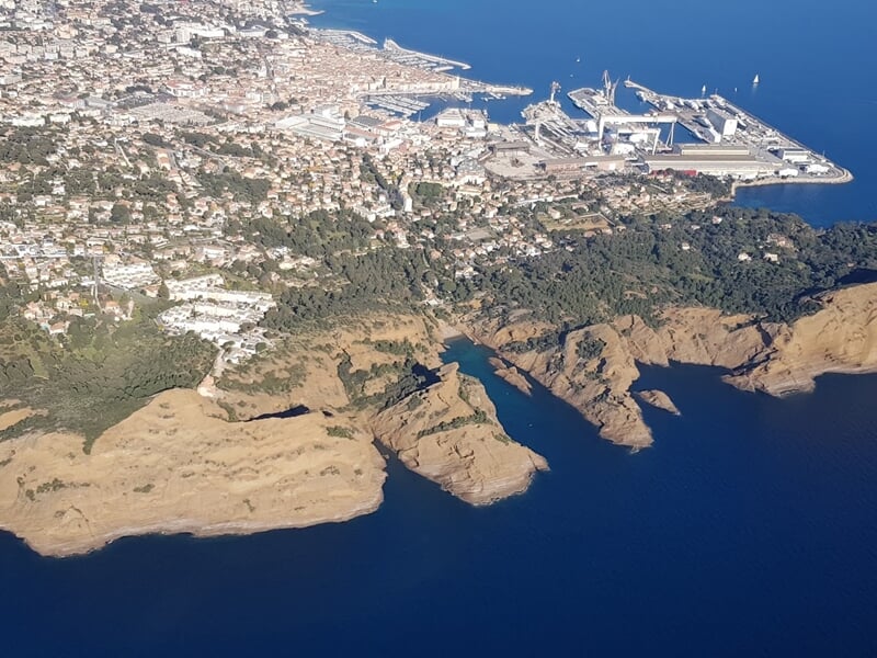 Vue aérienne du port industriel de La Ciotat, avec ses installations portuaires, la ville en arrière-plan, et les formations rocheuses côtières caractéristiques