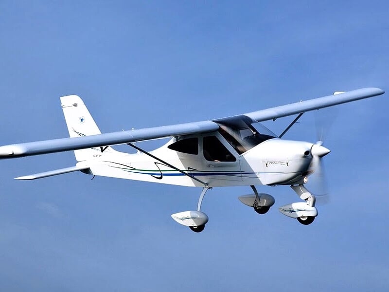 Petit avion de tourisme blanc en plein vol, avec un ciel bleu en arrière-plan, montrant l'élégance et la simplicité du design de l'appareil