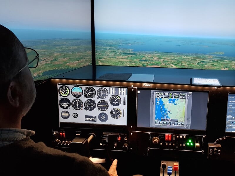 Pilote dans un simulateur d'avion regardant les instruments et un écran de navigation avec vue sur la mer.