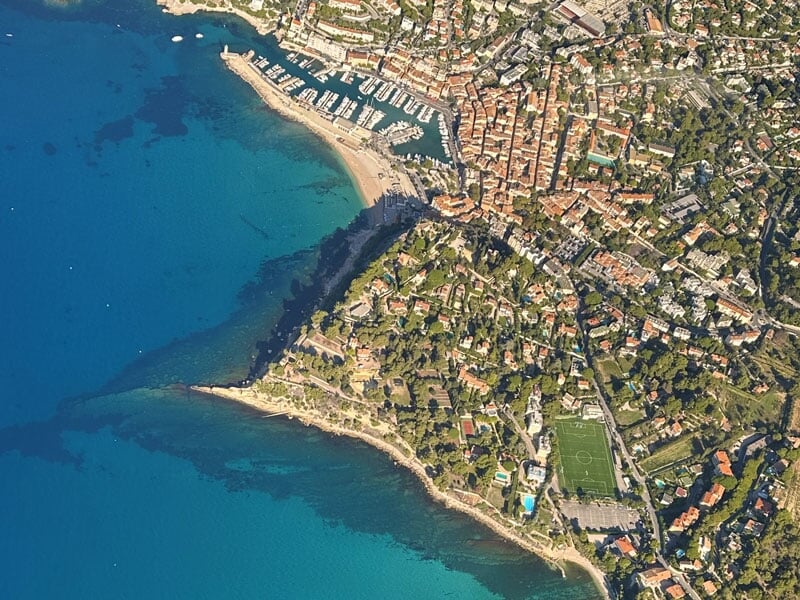 Vue aérienne de la ville côtière de Cassis avec son port de plaisance, ses toits en tuiles rouges et ses plages bordées d'eaux turquoise, entourée de collines verdoyantes