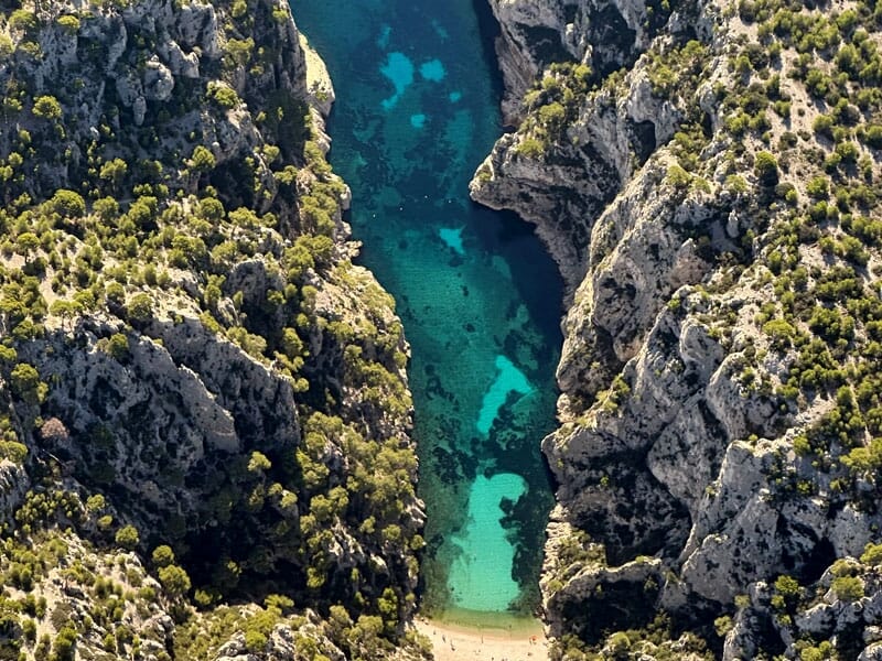 Calanque d'En-Vau près de Cassis, entourée de falaises calcaires escarpées et recouvertes de végétation méditerranéenne, avec une eau cristalline et des nuances de bleu et de vert