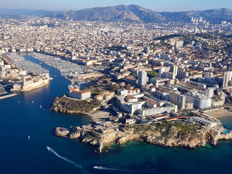 Vue panoramique de Marseille montrant le Vieux-Port avec ses yachts, la basilique Notre-Dame de la Garde en arrière-plan, et les collines environnantes