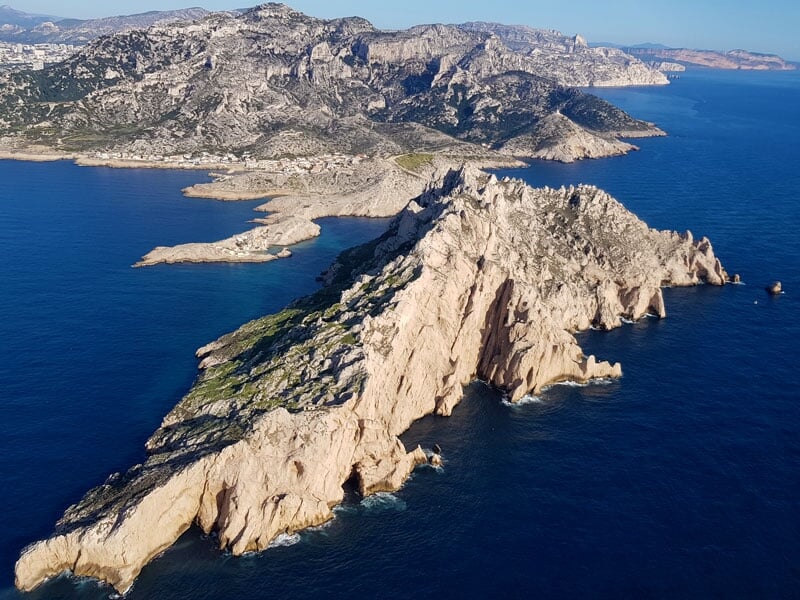 Pointe rocheuse escarpée de la Calanque de Sormiou, entourée de l'eau bleue profonde de la Méditerranée, avec des montagnes en arrière-plan