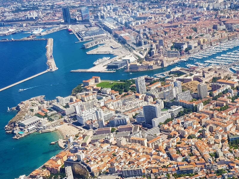 Vue aérienne du Vieux-Port de Marseille avec ses nombreux bateaux, les bâtiments modernes et historiques, et les infrastructures portuaires
