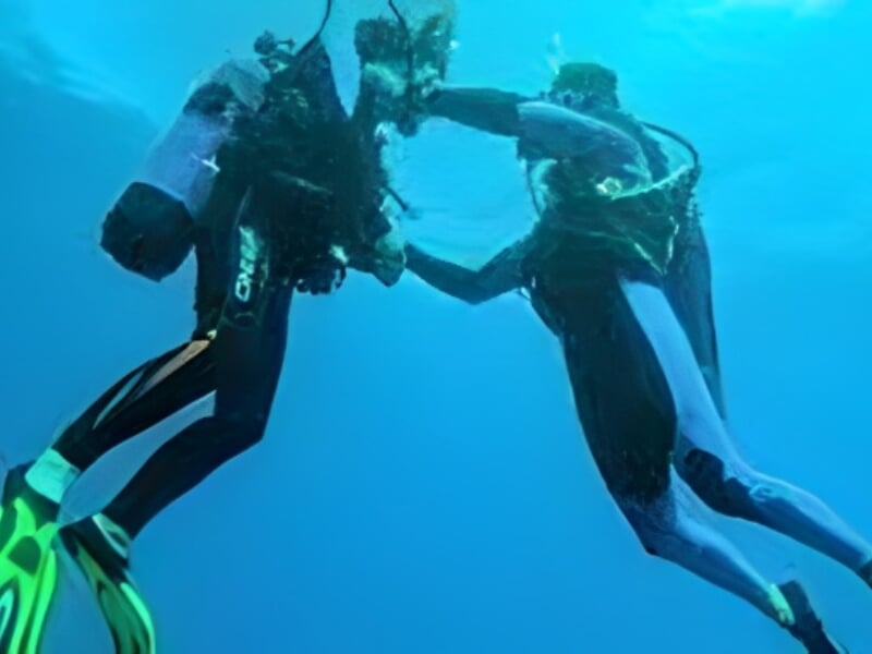 Deux plongeurs en position verticale sont immergés. L'un aide l'autre à adapter son matériel.