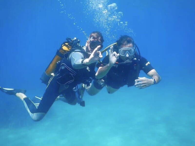 Deux plongeurs nageant sous l'eau et faisant un signe pour indiquer que tout va bien.
