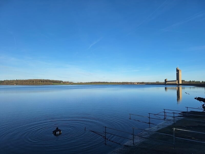 vue d'ensemble d'un lac articiel avec au loin sur la berge un édifice industriel.