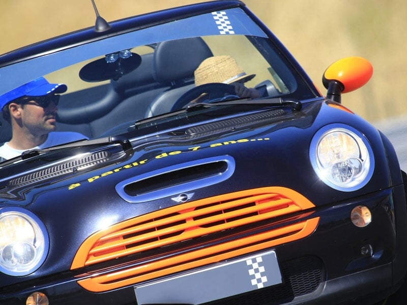 Conducteur et passager dans une voiture cabriolet noire avec détails orange, participant à une activité de pilotage, sur un circuit ensoleillé