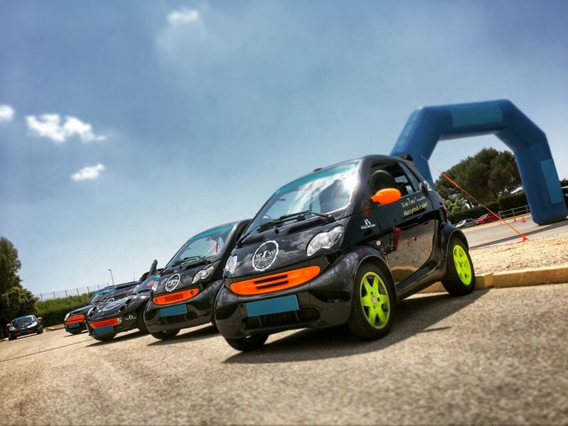 Petites voitures électriques noires avec des jantes vert fluo et des détails orange vifs, garées devant une arche gonflable sur un circuit automobile