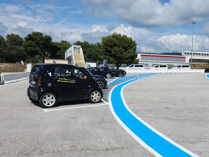 Voitures électriques noires alignées sur un parking, bordées par des lignes bleues marquant une piste, sous un ciel dégagé et entourées d’arbres