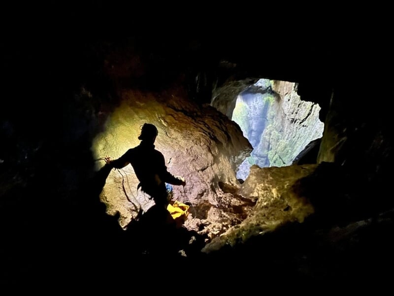ilhouette d'un spéléologue dans une grande caverne, éclairé par une lumière venant d'en haut, mettant en valeur les textures rocheuses autour.