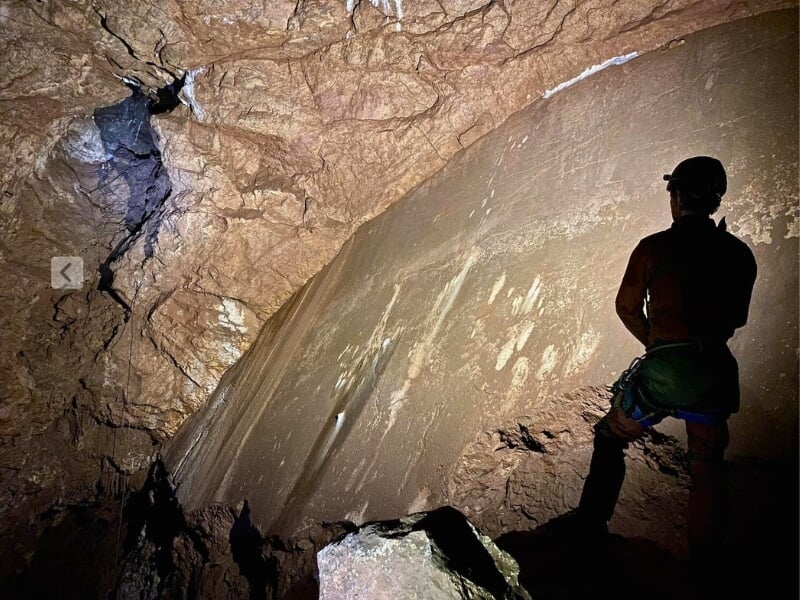 Un spéléologue observant de grandes parois rocheuses éclairées à l'intérieur d'une caverne sombre.