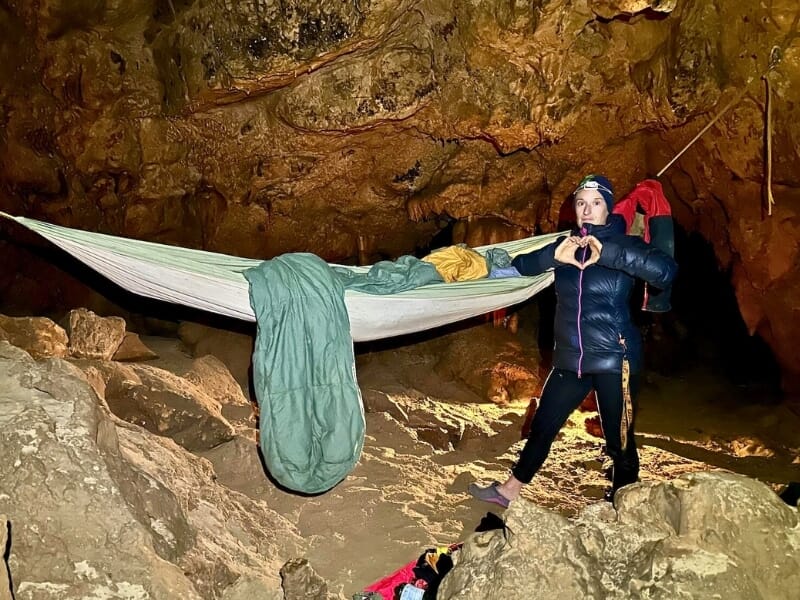 Spéléologue à côté d'un hamac suspendu dans une grotte, faisant un signe de cœur avec les mains