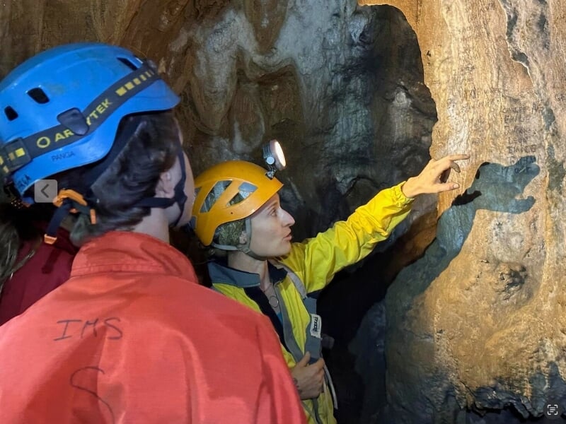 Deux spéléologues examinant de près les formations rocheuses à l'intérieur d'une grotte, éclairés par une lampe frontale.