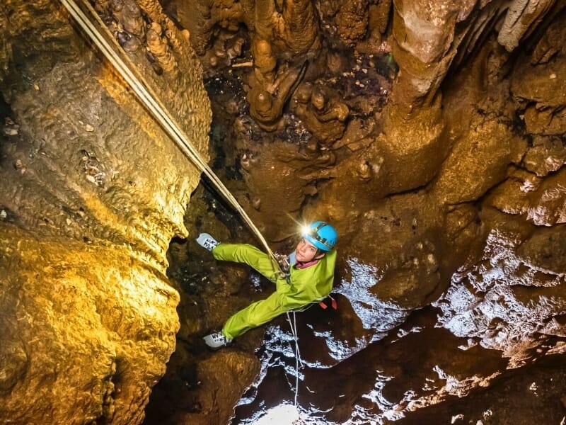 Spéléologue descendant en rappel une paroi rocheuse dans une grande caverne, avec des équipements d'escalade