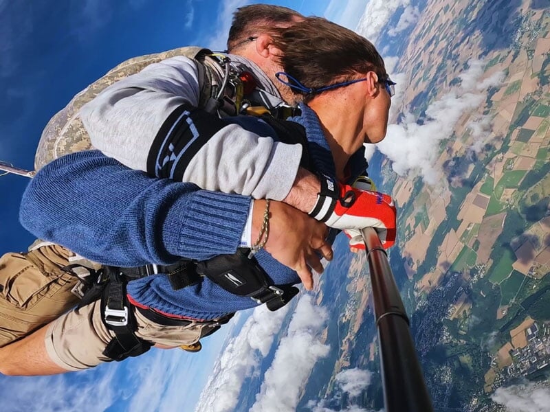 Tandem de parachutisme en plein vol, vue plongeante sur la campagne avec champs et nuages. Perspective spectaculaire et sensation de liberté en altitude