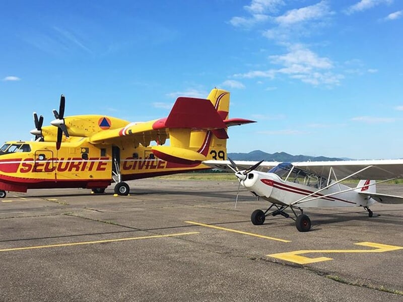 Deux avions stationnés sur une piste, un avion de la sécurité civile jaune et un petit avion blanc et rouge.