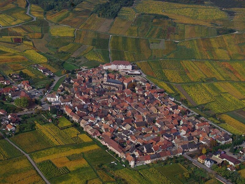 Vue aérienne d'un village entouré de champs et de vignes, avec des maisons aux toits rouges.