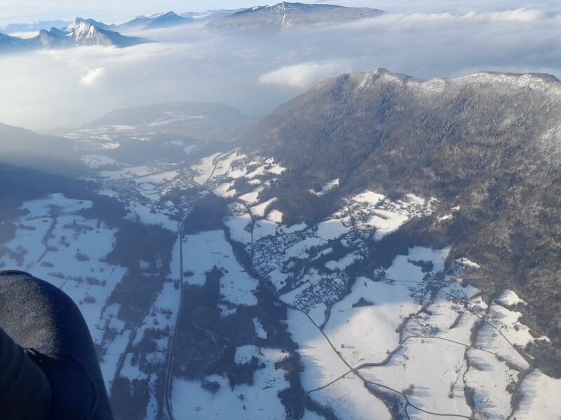 Vue aérienne de montagnes enneigées et de vallées, montrant des champs partiellement recouverts de neige et des routes serpentant à travers le paysage.