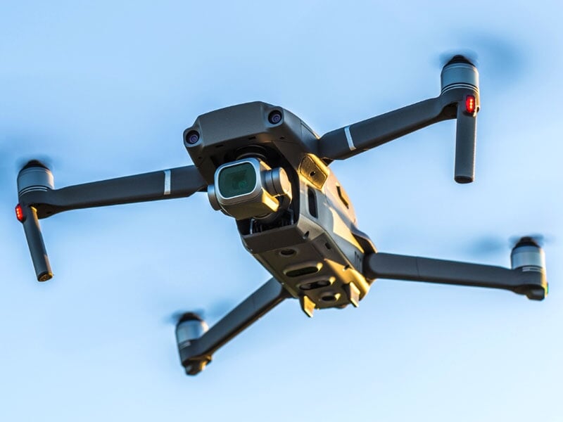 Drone professionnel noir en vol avec caméra visible, ciel bleu en arrière-plan