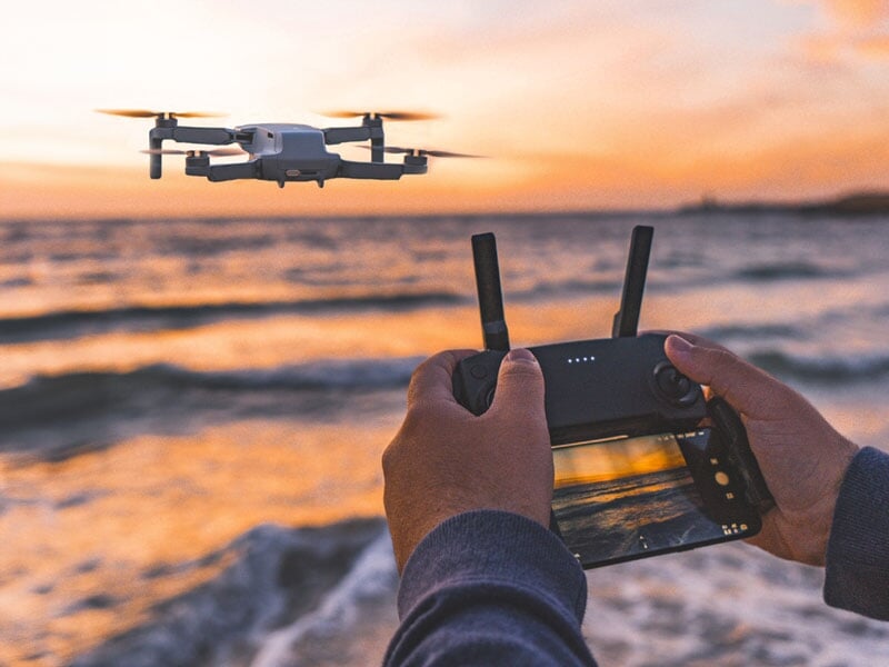 Mains tenant une télécommande de drone, vol en bord de mer au crépuscule