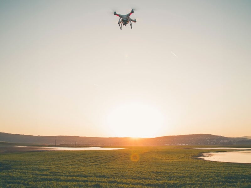 Drone quadricoptère survolant un champ au coucher du soleil, paysage agricole en contre-jour