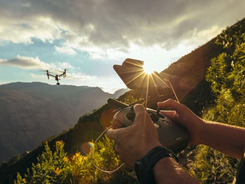 Pilote de drone contrôlant un vol en montagne, soleil couchant en arrière-plan