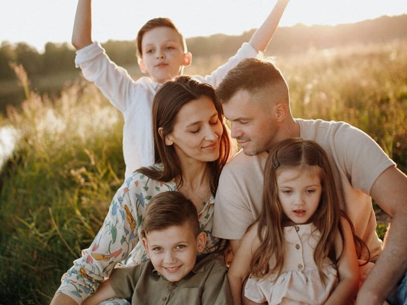 Une famille heureuse avec deux enfants posant dans un champ au coucher du soleil, ambiance chaleureuse et naturelle.