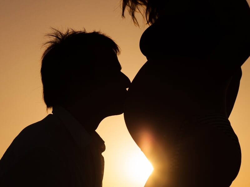 Silhouette d'un homme embrassant le ventre arrondi de sa femme enceinte au coucher du soleil, moment tendre et intime.