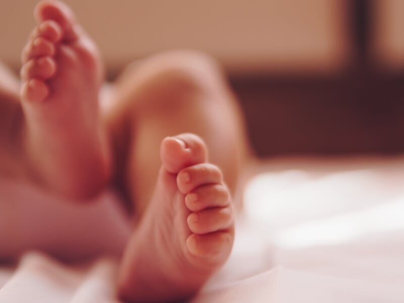 Gros plan sur les petits pieds d'un bébé allongé sur un lit, éclairage doux et ambiance chaleureuse.