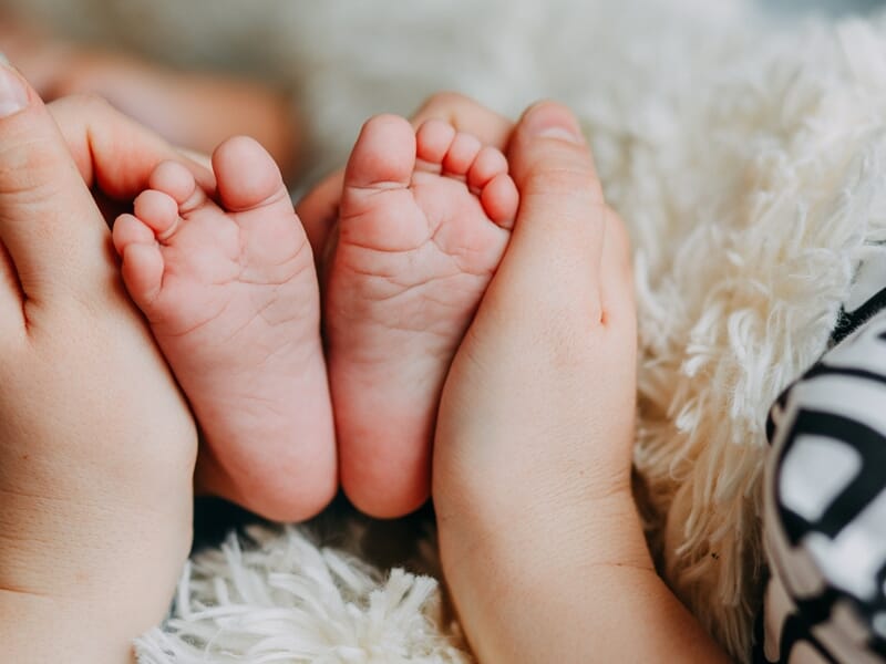 Petits pieds de bébé tenus par des mains d'adulte sur un tissu blanc, symbolisant la douceur et la protection.