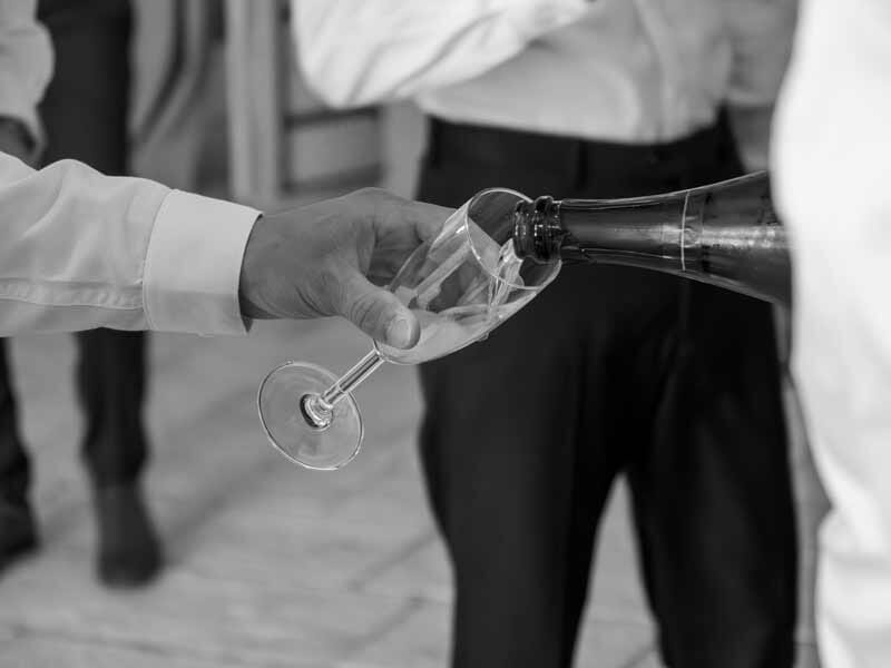 Main versant du champagne dans une flûte lors d'une célébration, ambiance festive en noir et blanc.