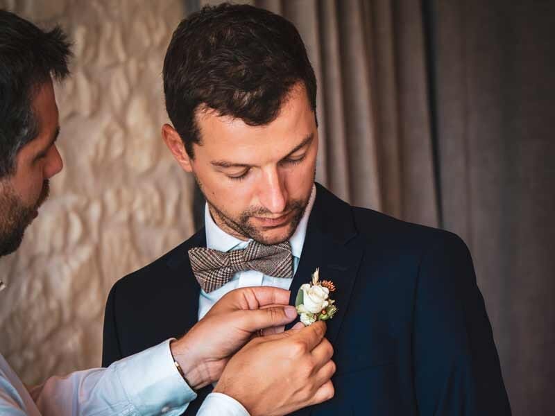 Homme en costume ajustant une boutonnière sur son veston, préparatifs pour un événement formel.