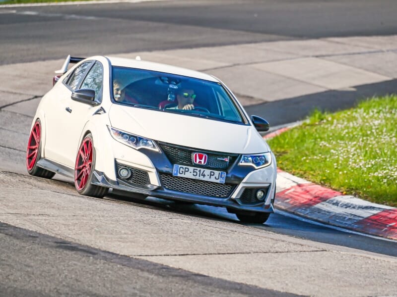 Honda Civic Type R blanche prise en action à un virage serré sur circuit, montrant l'avant du véhicule avec des jantes rouges et un design agressif.