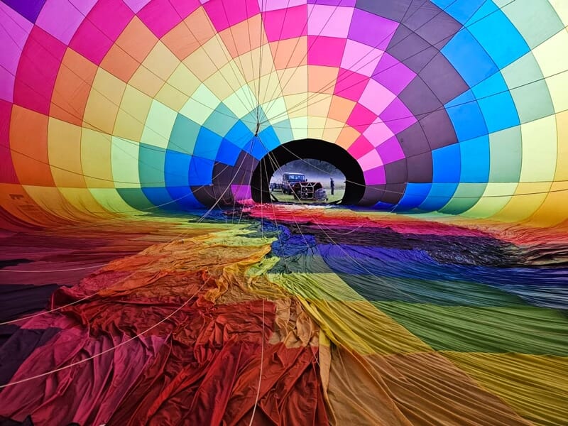 Intérieur d'une montgolfière multicolore en cours de gonflage avec un véhicule visible à travers l'ouverture.