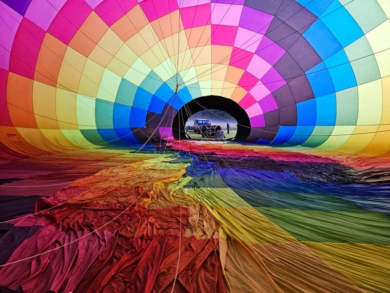 Intérieur d'une montgolfière multicolore en cours de gonflage avec un véhicule visible à travers l'ouverture.