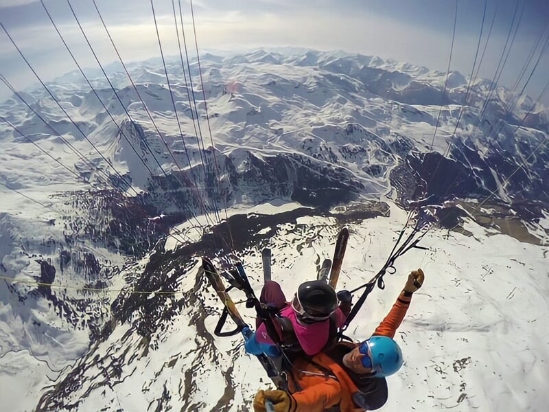 Parapente en tandem avec deux personnes survolant un paysage montagneux enneigé