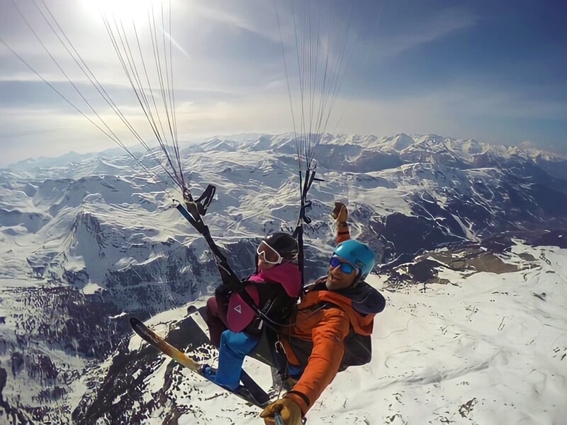 Parapente avec deux personnes en tandem volant au-dessus d'une station de ski en hiver