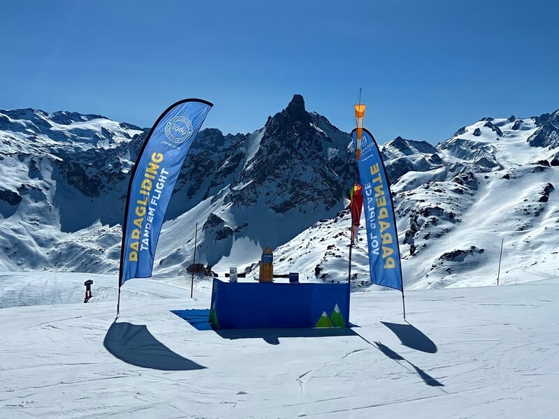 Parapente en tandem avec deux skieurs volant au-dessus d'un paysage enneigé et boisé