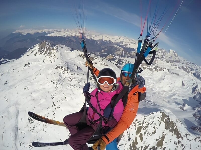 Parapente avec deux personnes en tandem survolant une vallée enneigée et des montagnes