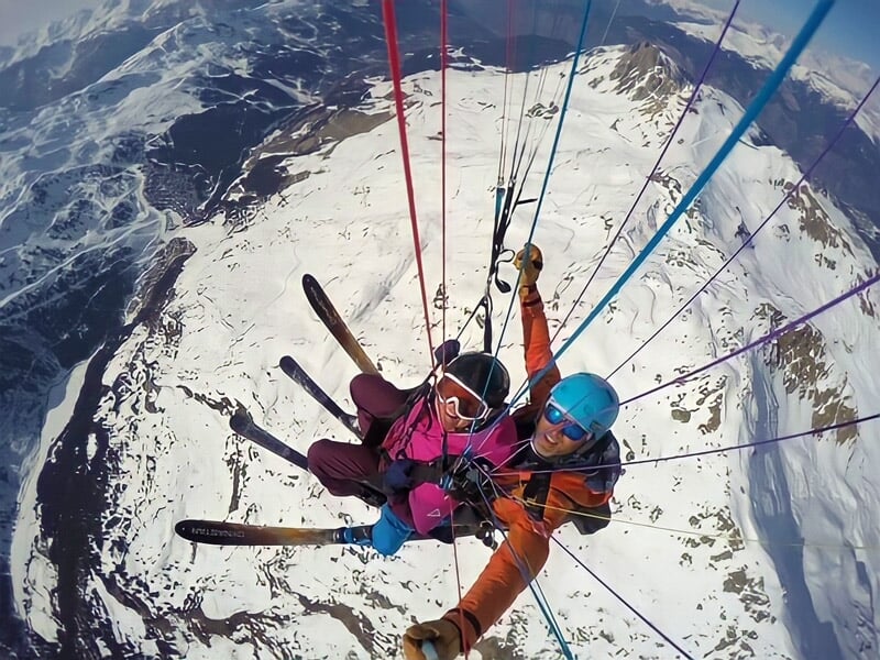 Parapente en tandem avec deux skieurs volant au-dessus d'une station de ski en montagne