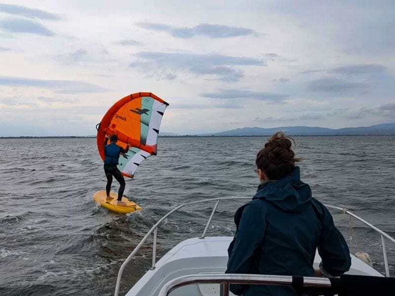 Personne pratiquant le wingfoil sur une planche jaune avec une aile orange sur l'eau agitée au large.