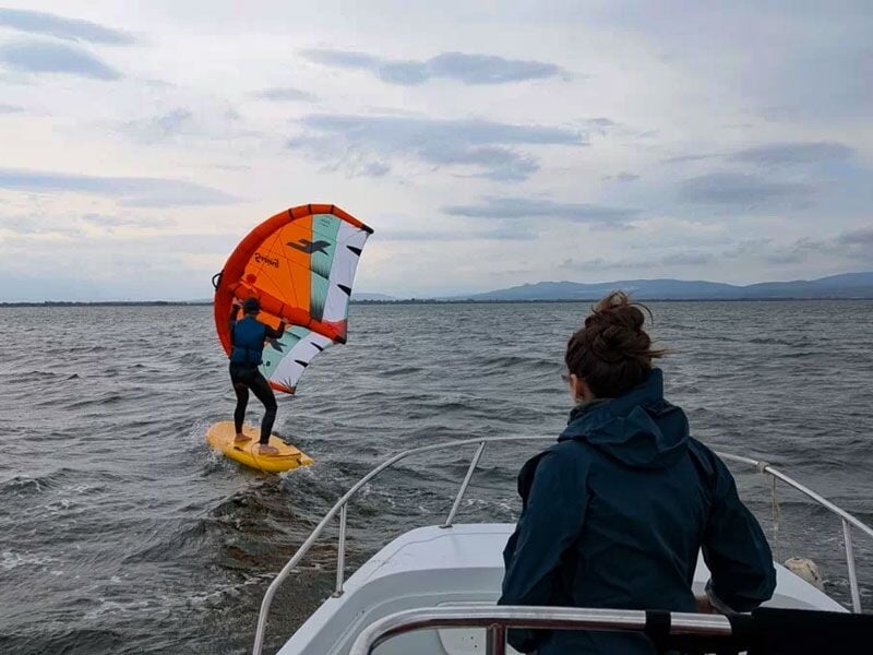 Personne pratiquant le wingfoil sur une planche jaune avec une aile orange sur l'eau agitée au large.